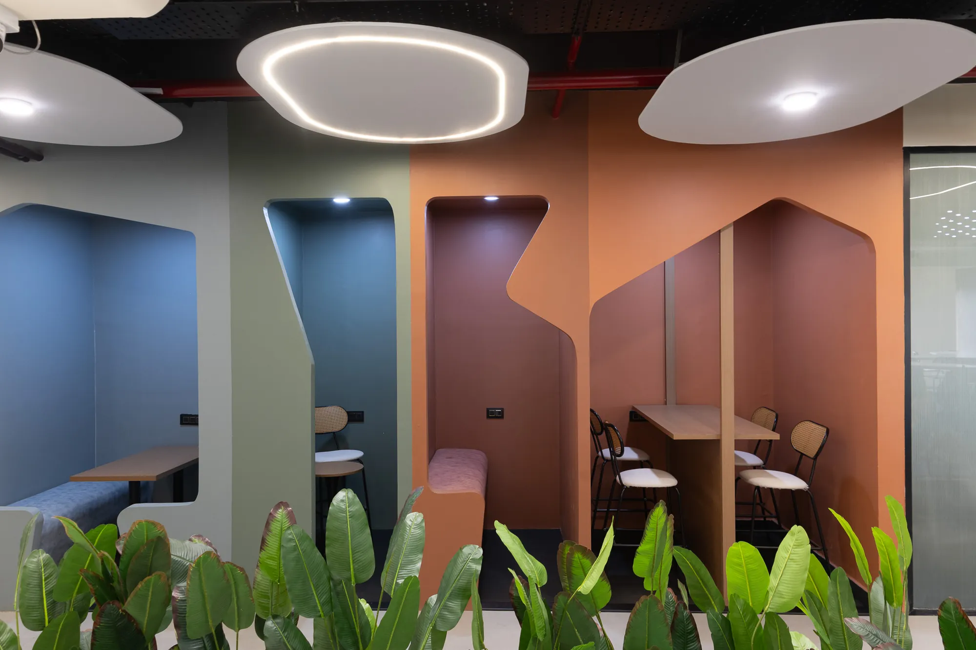 Colour-blocked phone booths in blue, sage and terracotta beneath oval ceiling lights