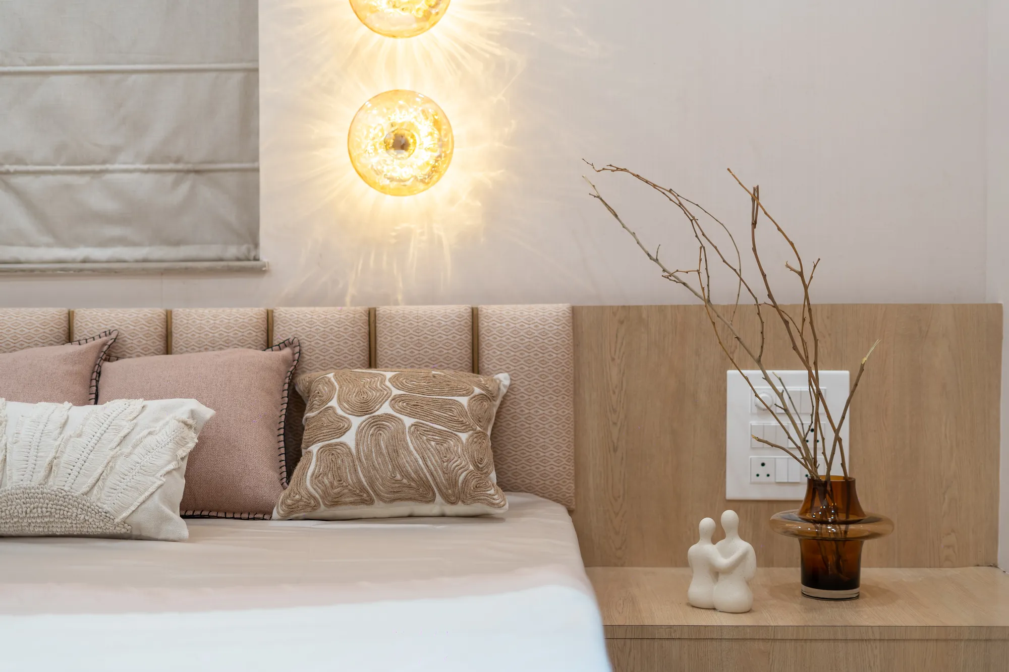 Bedside detail with a panelled headboard, cushions and a warm wall light