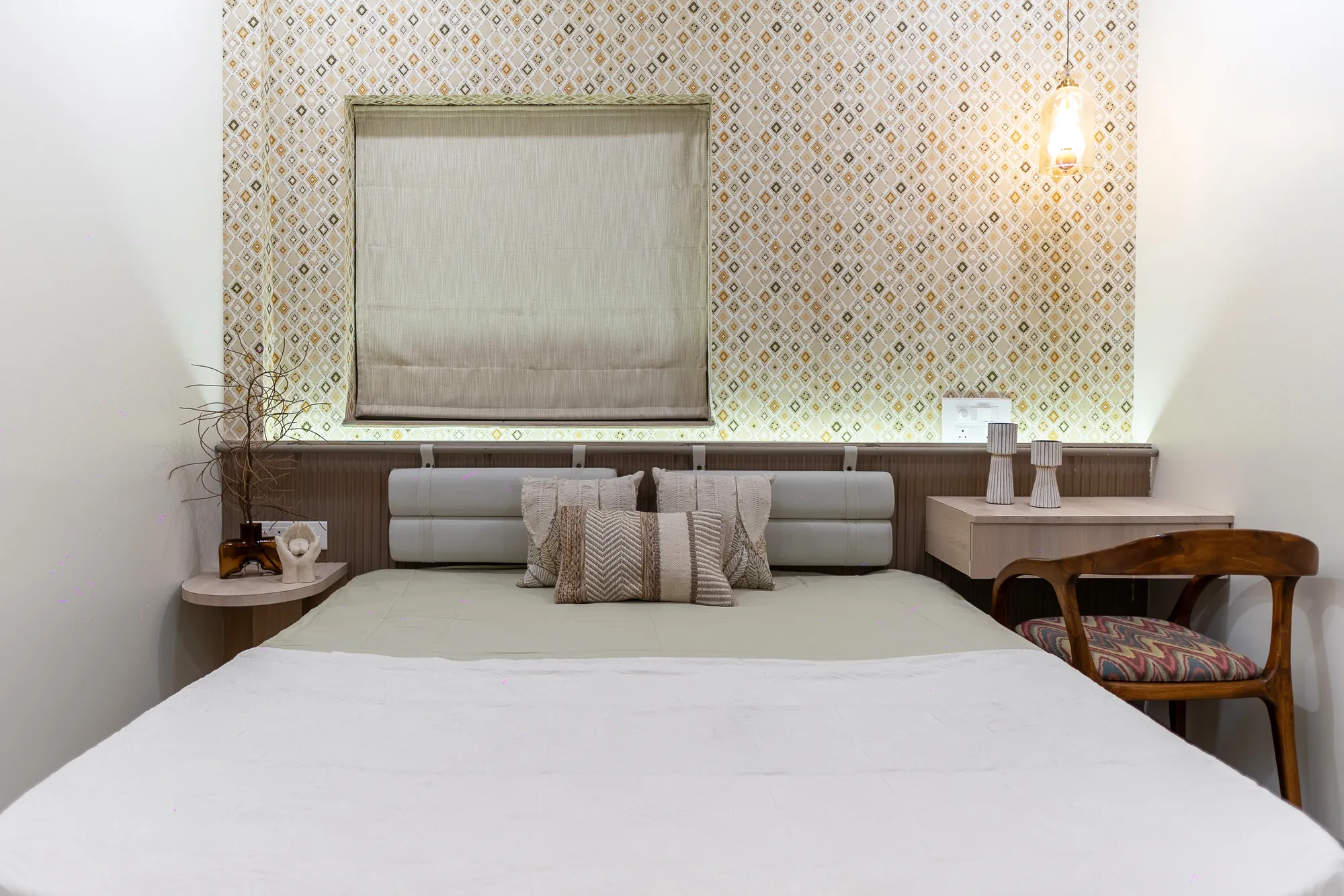 Bedroom with a patterned wall behind the bed, upholstered headboard and wooden side chair