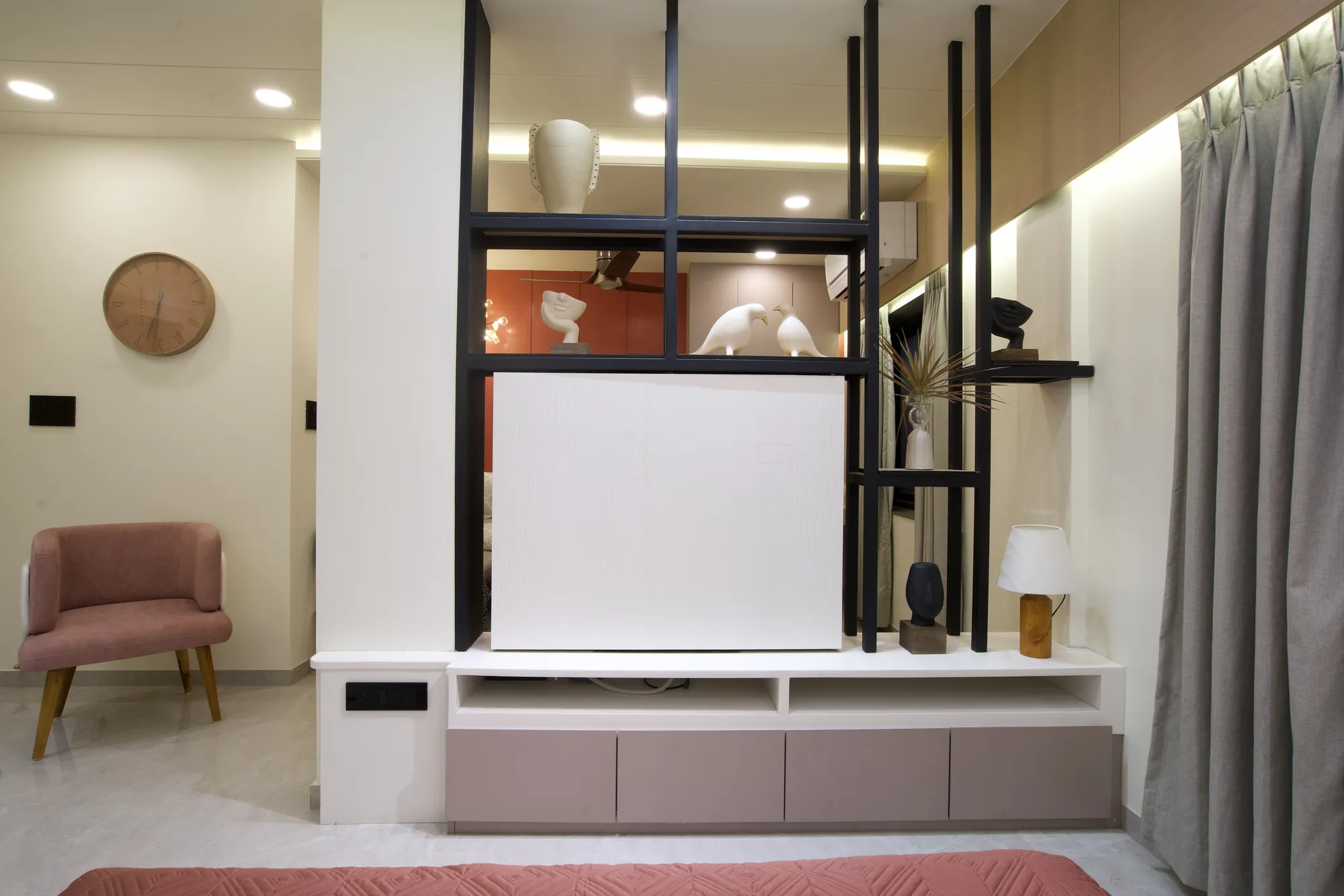 Bedroom partition with black-framed shelving, looking through to the coral living area