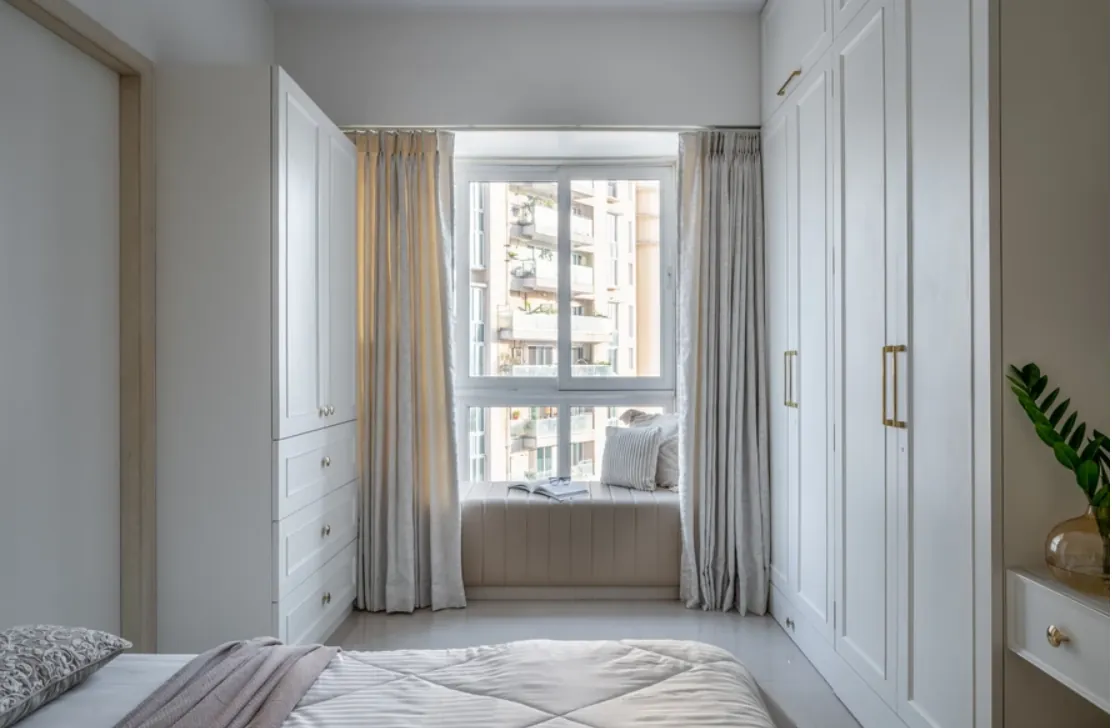 Bedroom window seat framed by white wardrobes and sheer curtains