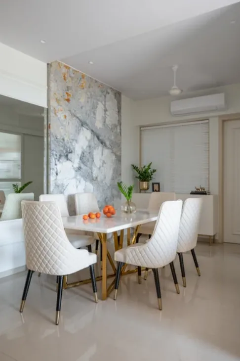 Dining table with white upholstered chairs in front of a grey-veined stone feature wall